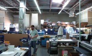 Glassical Designs production team member working in a modern corporate awards manufacturing facility, surrounded by precision equipment, custom packaging, and acrylic material used in high-end recognition awards.